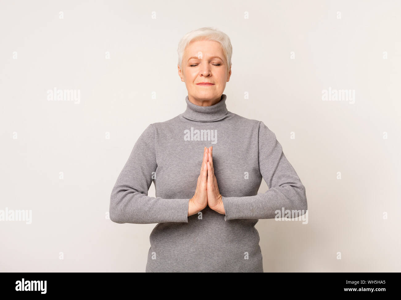 Elderly woman meditating indoors showing namaste gesture Stock Photo