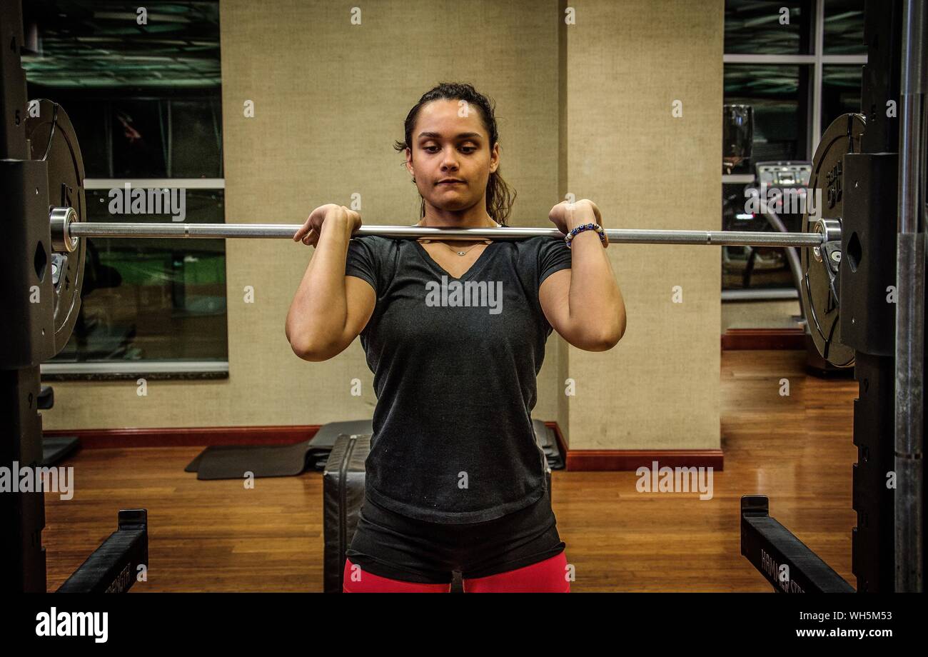 Determined Young Woman Lifting Barbell At Gym Stock Photo