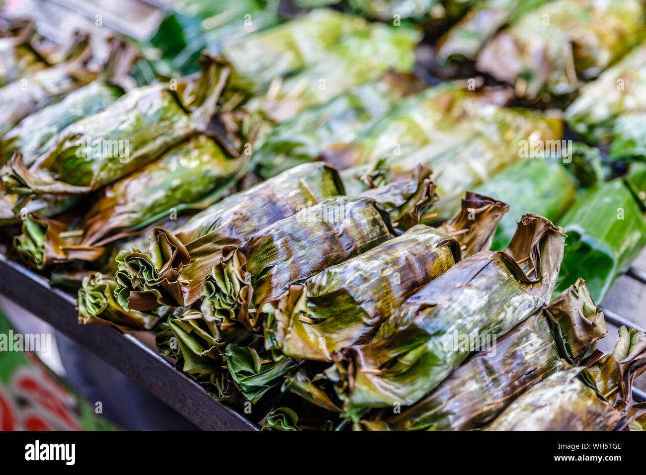 Grilled sticky rice with coconut milk and taro or banana wrapped in banana leaves. Thai street food, Thai traditional dessert. Bangkok, Thailand Stock Photo