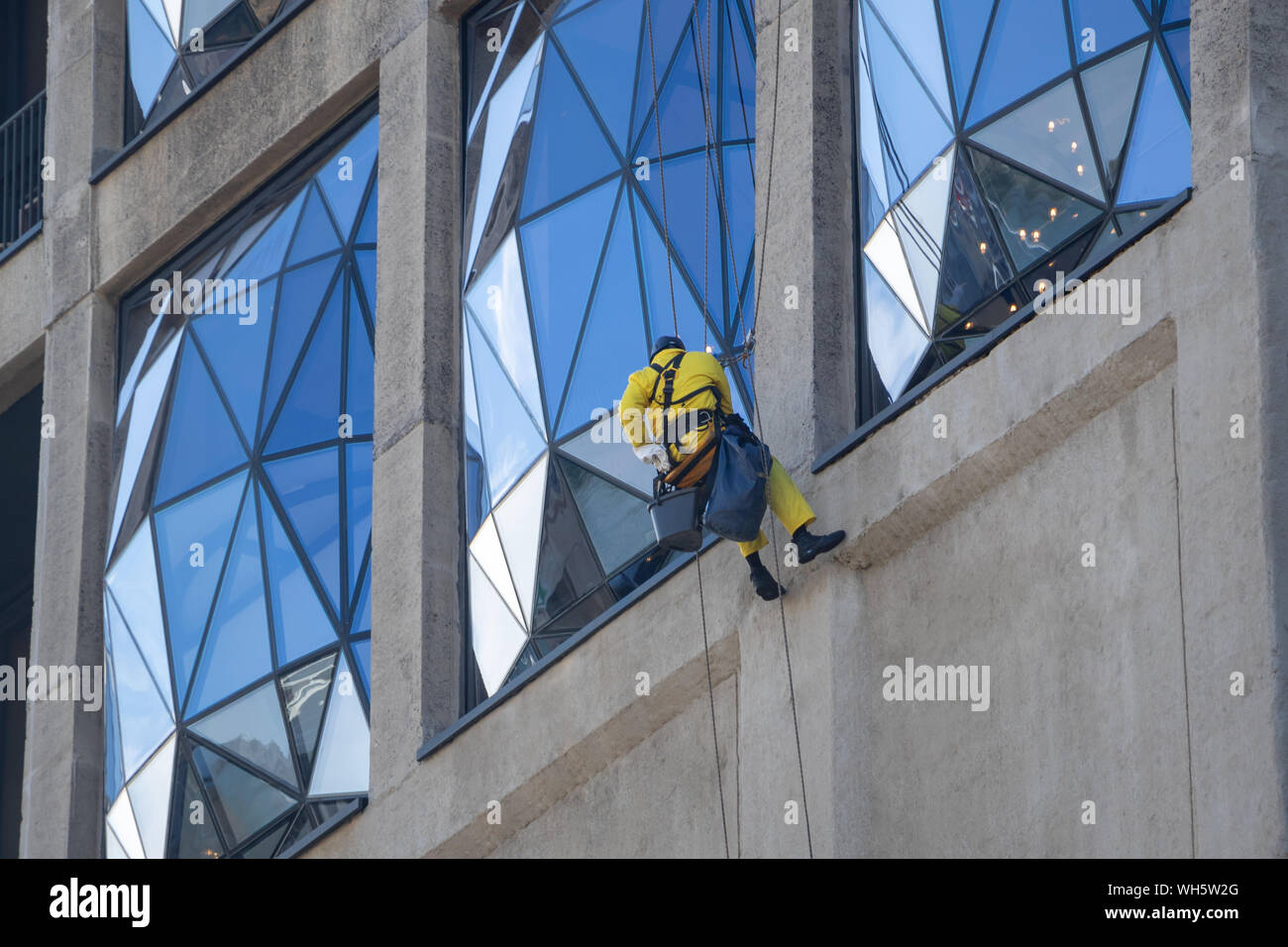 window washer dressed in yellow protective clothing, climbing on a modern building Stock Photo