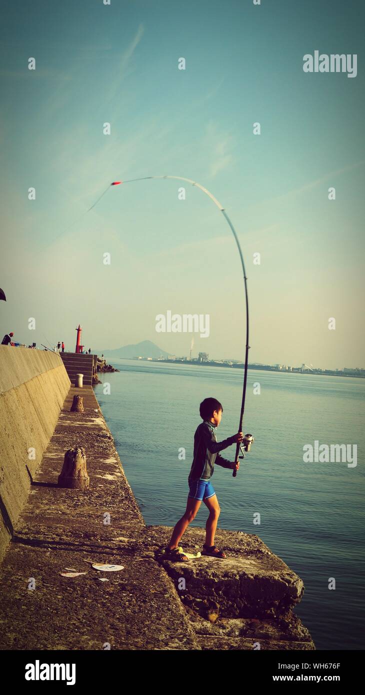 Side View Of Boy Casting Fishing Line In Sea Stock Photo