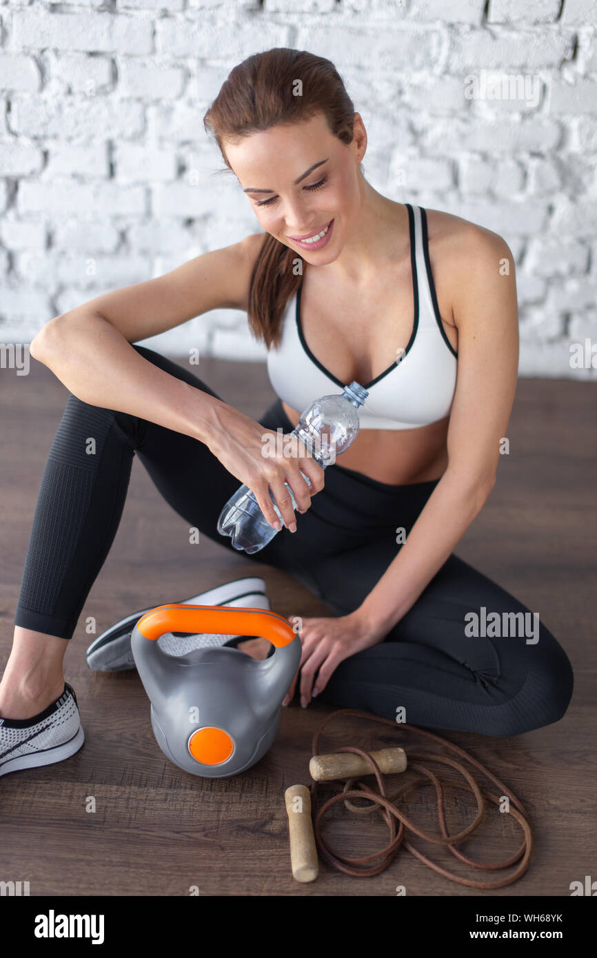 Tired woman hydrating after workout, looking down and smiling Stock Photo