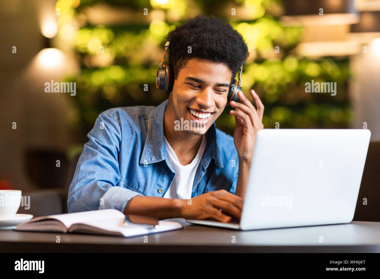 Cheerful teen guy with headset looking at laptop Stock Photo