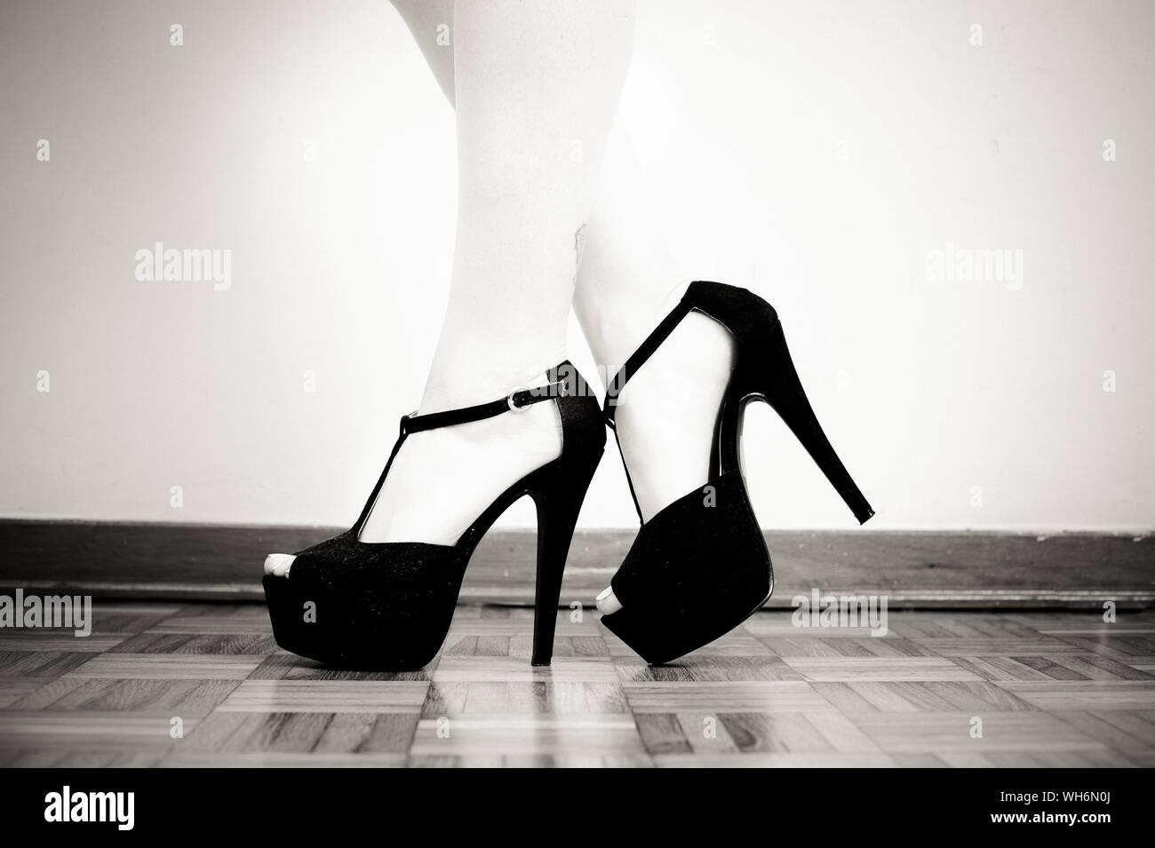 Low Section Of Woman Wearing High Heels On Hardwood Floor Against Wall Stock Photo
