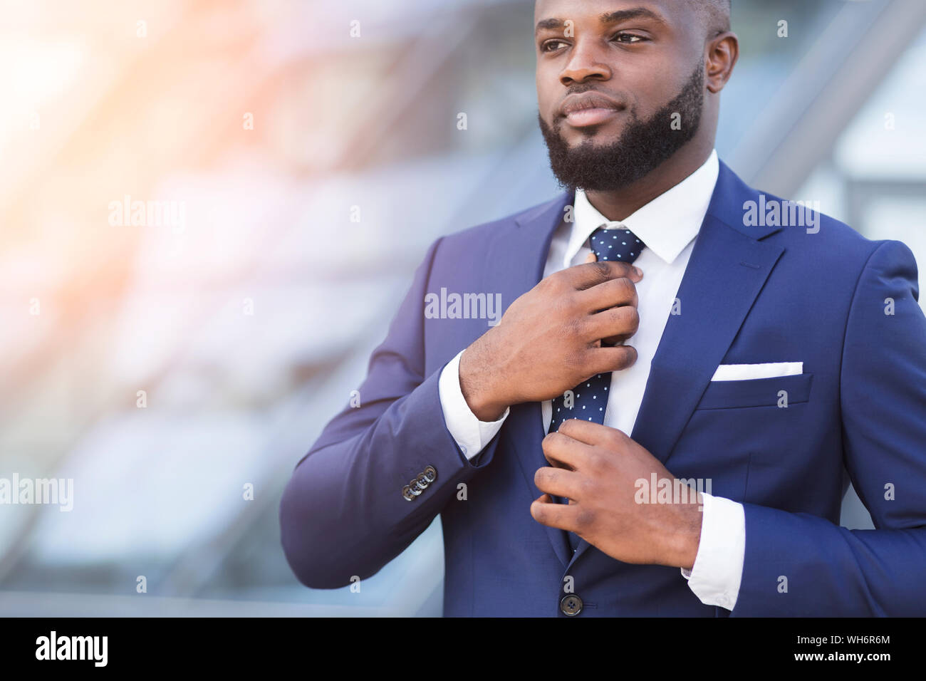 Young Black Businessman Adjusting Necktie In Urban Area Stock Photo