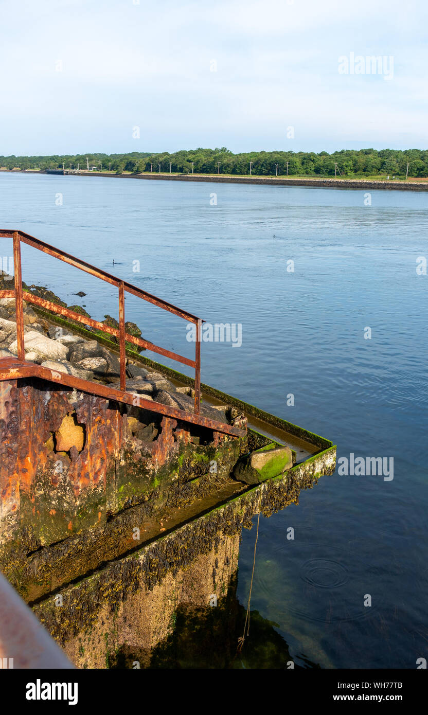 Rusting steel railing & retaining wall with holes from salt water and covered with barnacles and green algae along the Cape Cod Canal Stock Photo