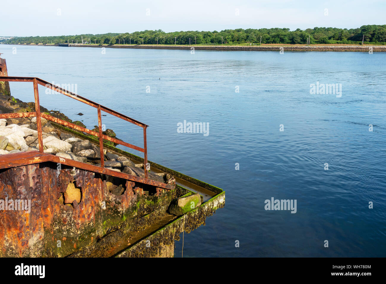Rusting steel railing and retaining wall with holes, seaweed, barnacles ...