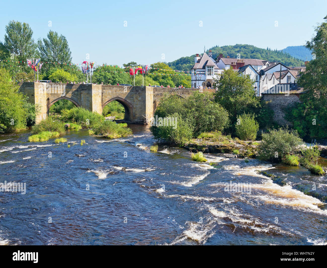 The fast flowing River Dee flows through the old stone bridge, draped in bunting and flags, in Llangollen, Wales Stock Photo