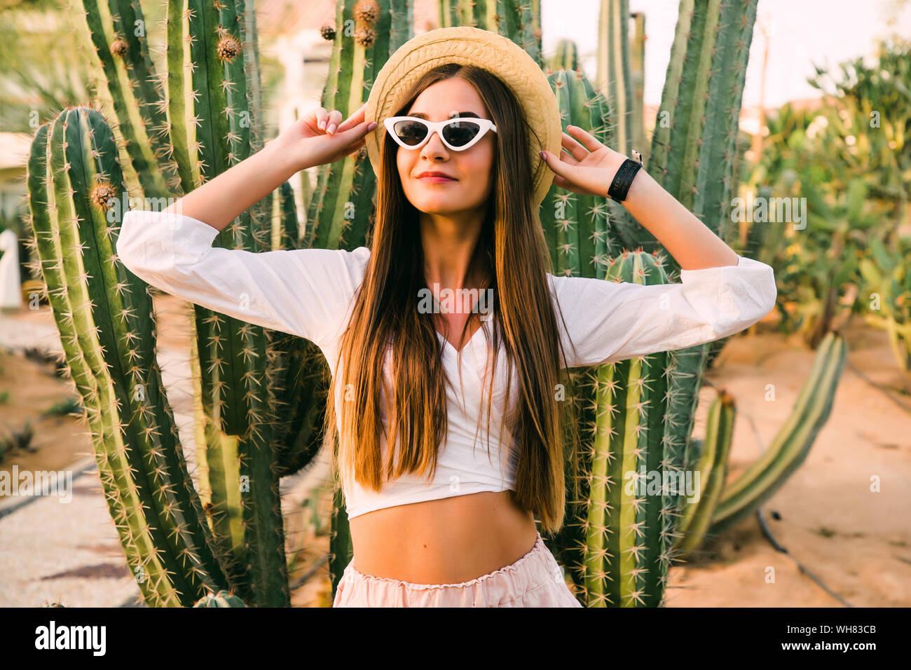Hippie woman in long pink skirt walking near big cactuses Stock Photo
