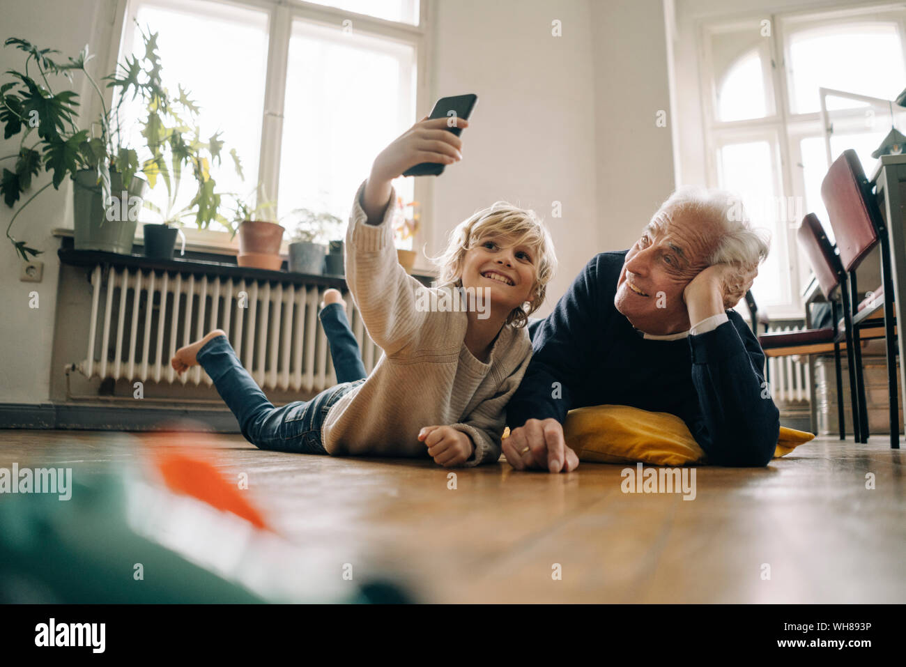 Grandfather and grandson lying on the floor at home taking a selfie Stock Photo