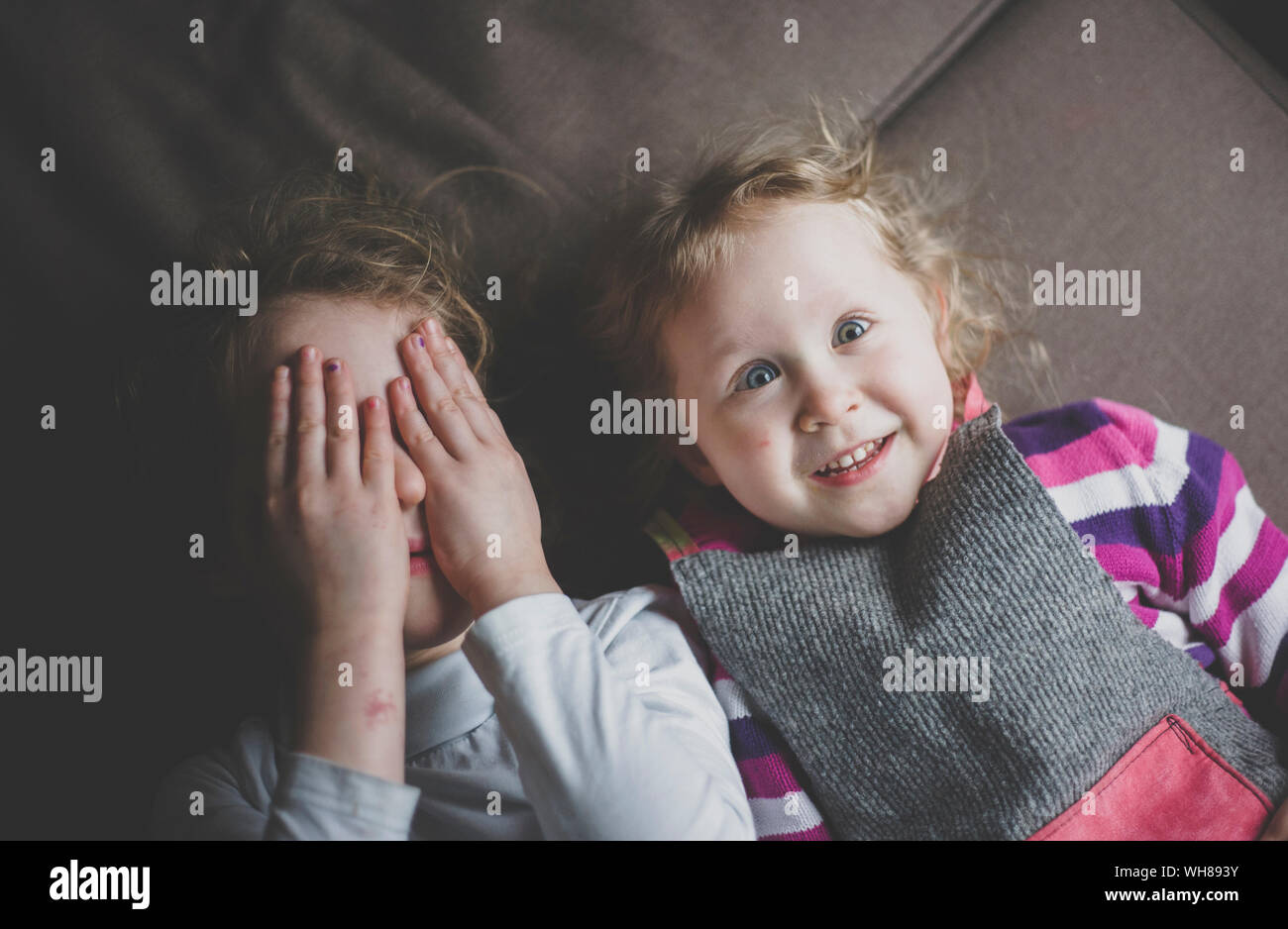 Portrait of two little sisters lying on couch having fun, top view Stock Photo