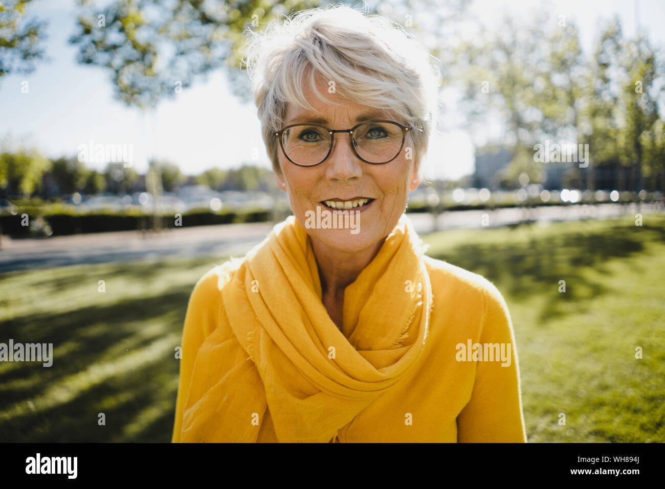 Portrait of smiling mature woman with grey hair wearing glasses and yellow clothes Stock Photo
