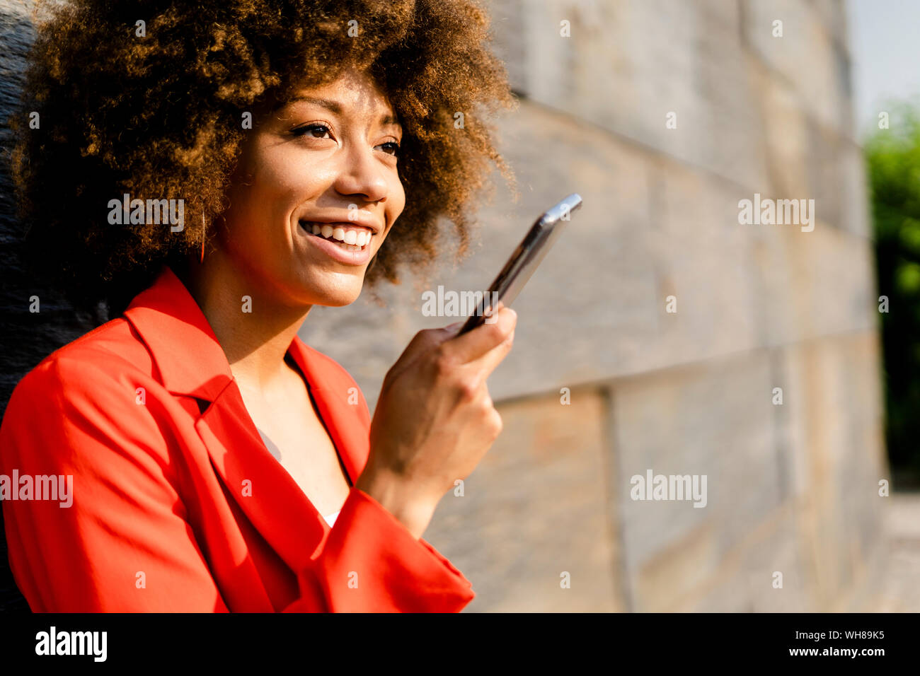 Portrait of smiling young woman on the phone wearing fashionable red suit jacket Stock Photo