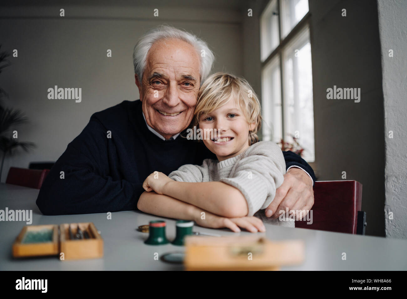 Portrait of happy watchmaker and his grandson sitting at table Stock Photo