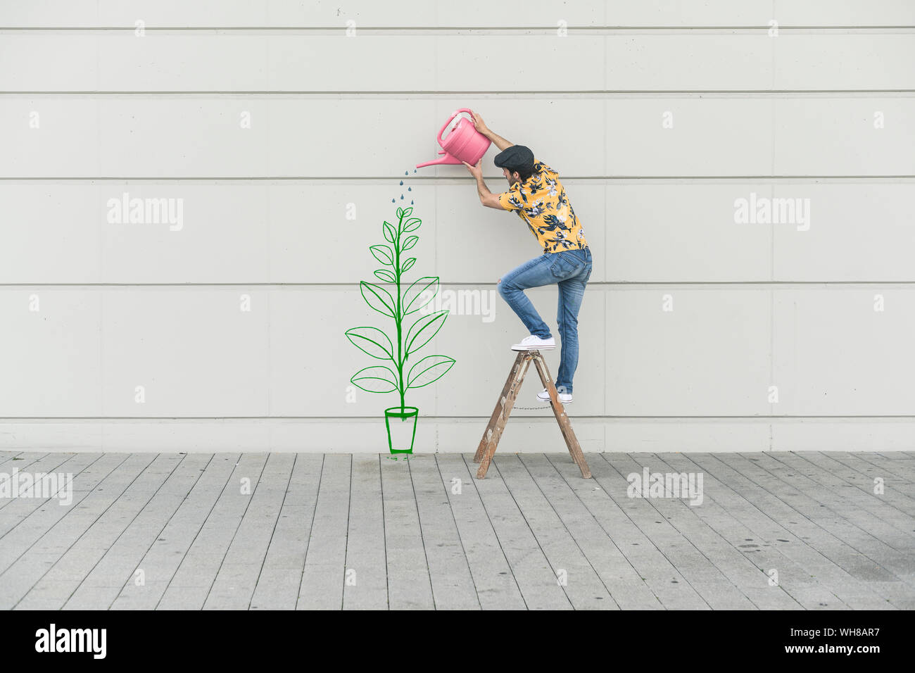 Digital composite of young man watering flower at a wall Stock Photo