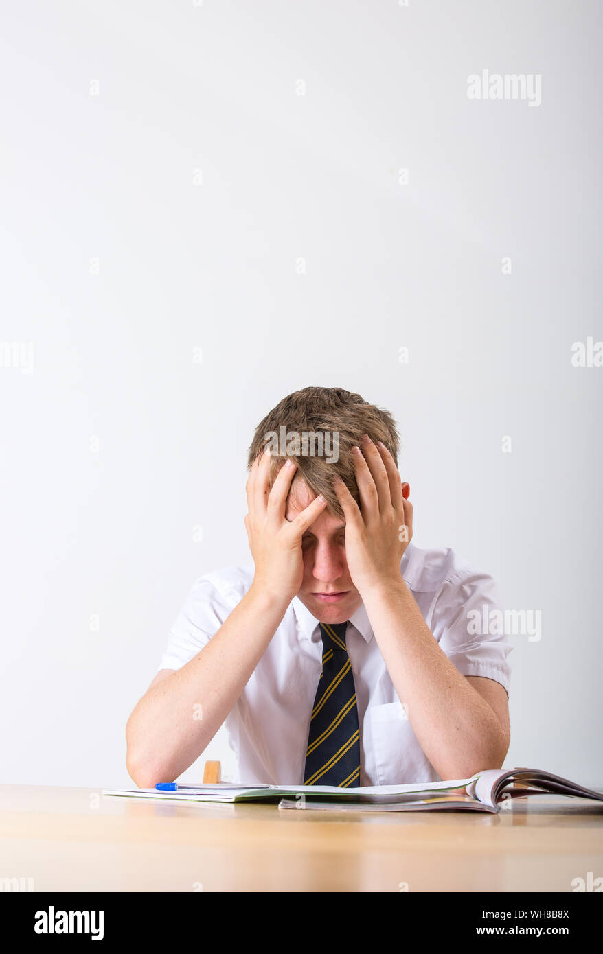 A stressed school pupil with his head in his hands sat at his desk Stock Photo