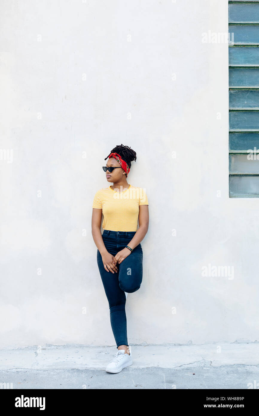 Young woman wearing hair-band and sunglasses leaning against white wall Stock Photo