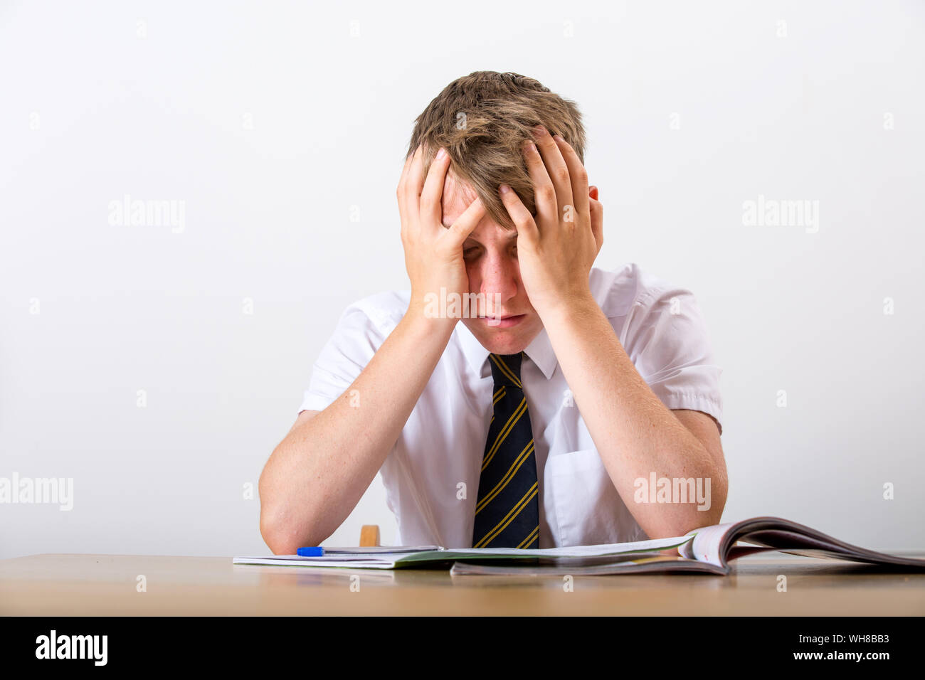 A stressed school pupil with his head in his hands sat at his desk Stock Photo