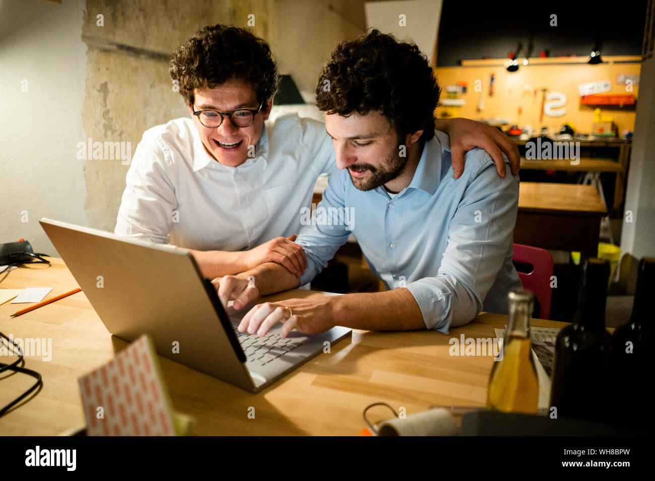 Two happy colleagues using laptop in the dark together Stock Photo