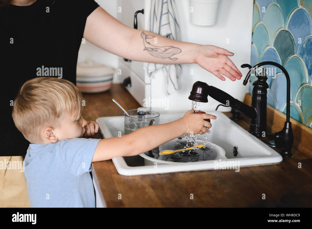 Little boy washing peach in the kitchen with his mother's help Stock Photo
