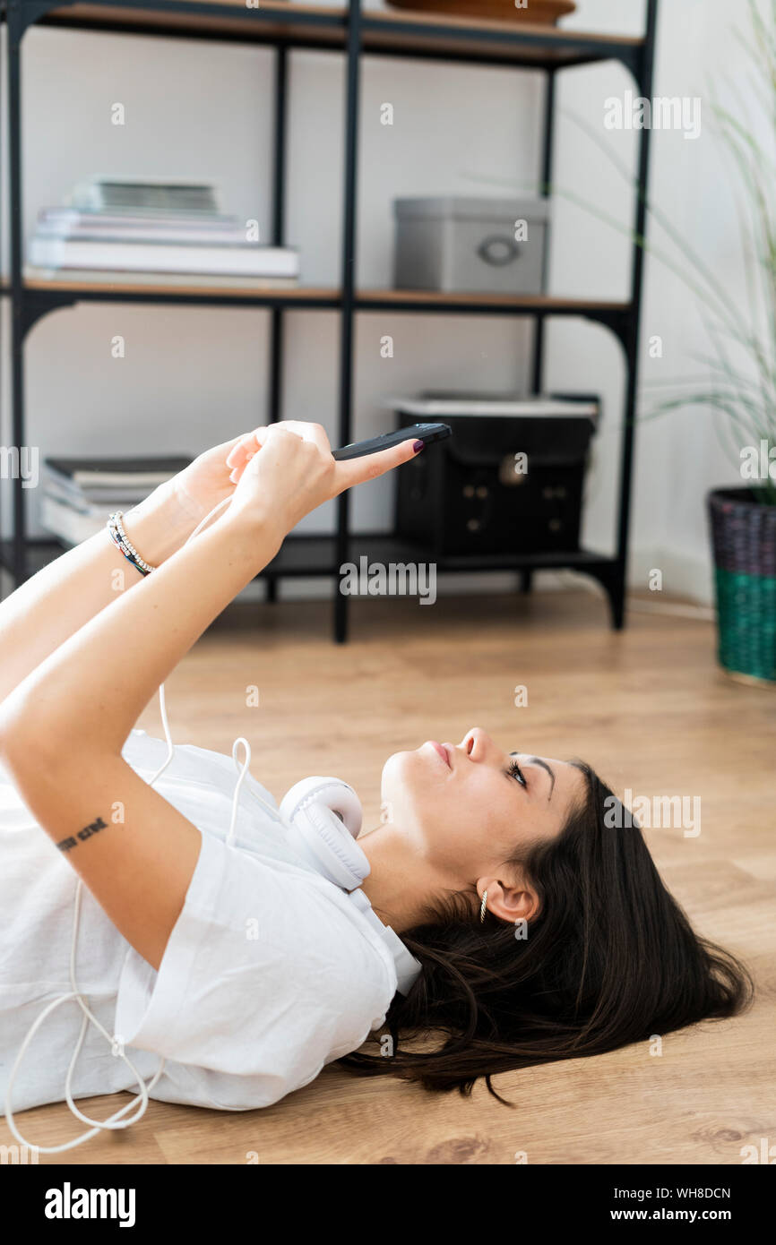 Young woman lying on the floor holding smartphone Stock Photo