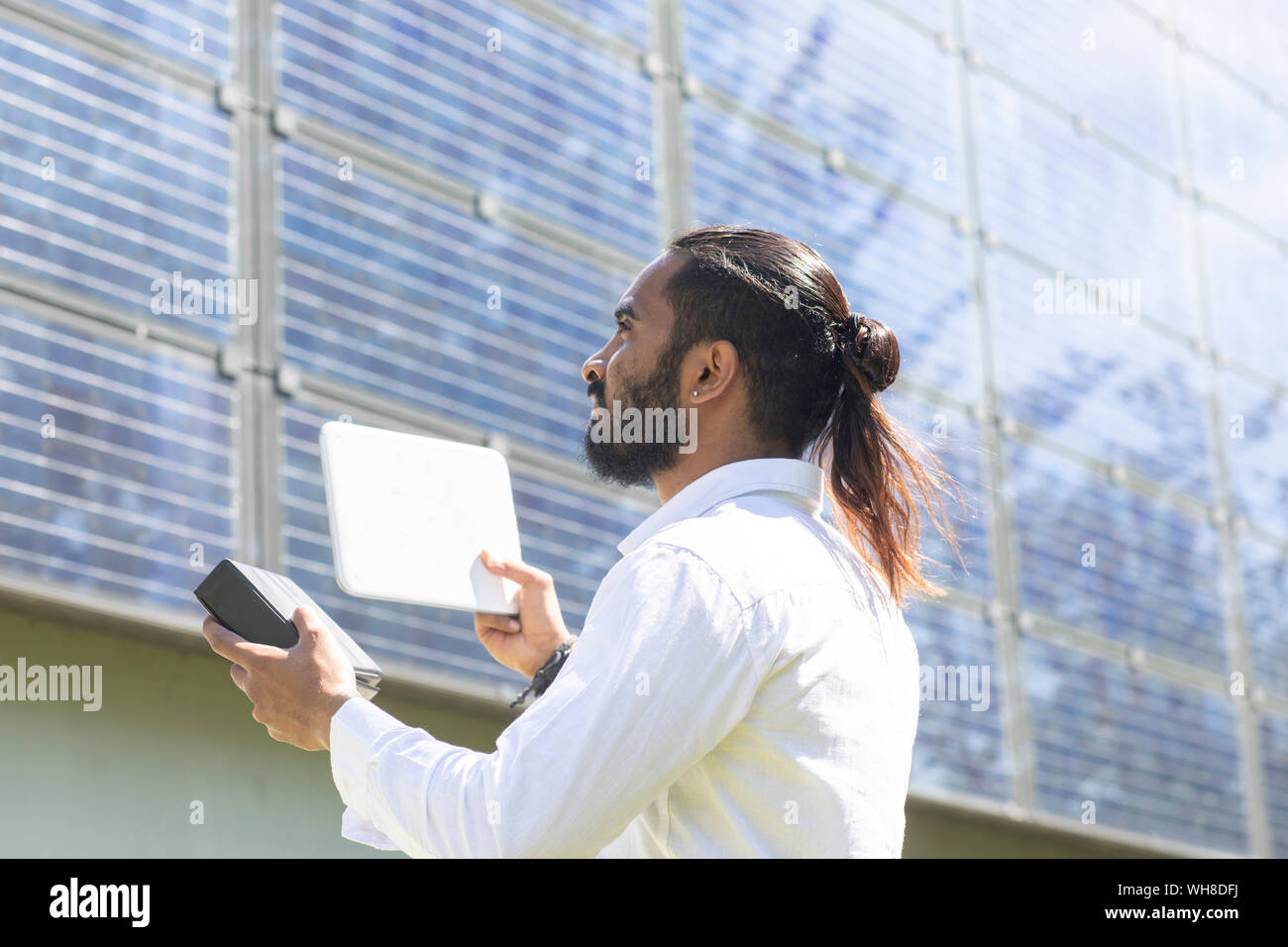 Bearded young man measuring photovoltaic plant on house facade Stock Photo