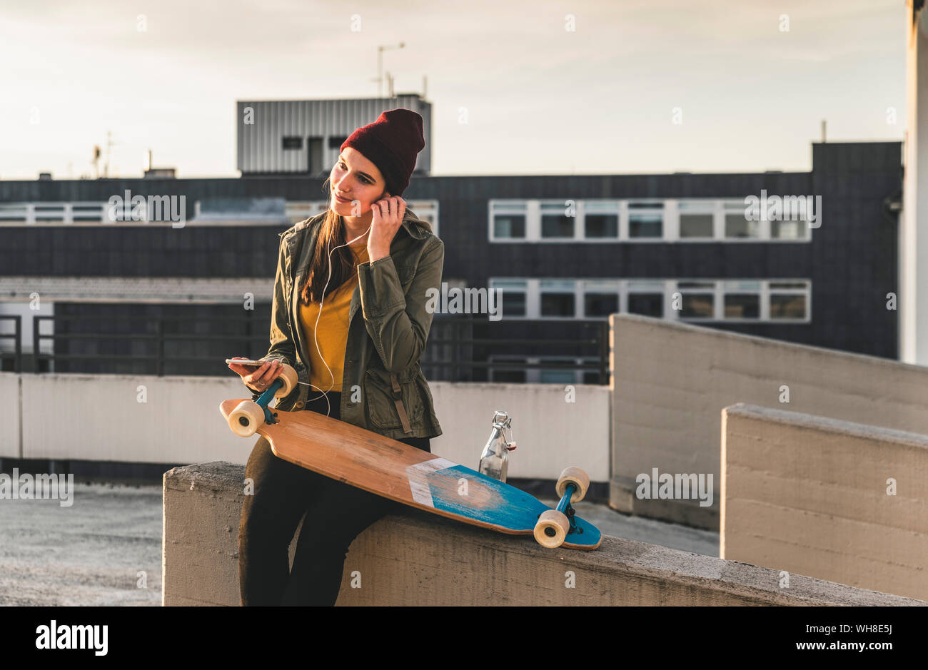 Stylish young woman with skateboard, earphones and cell phone on parking deck Stock Photo