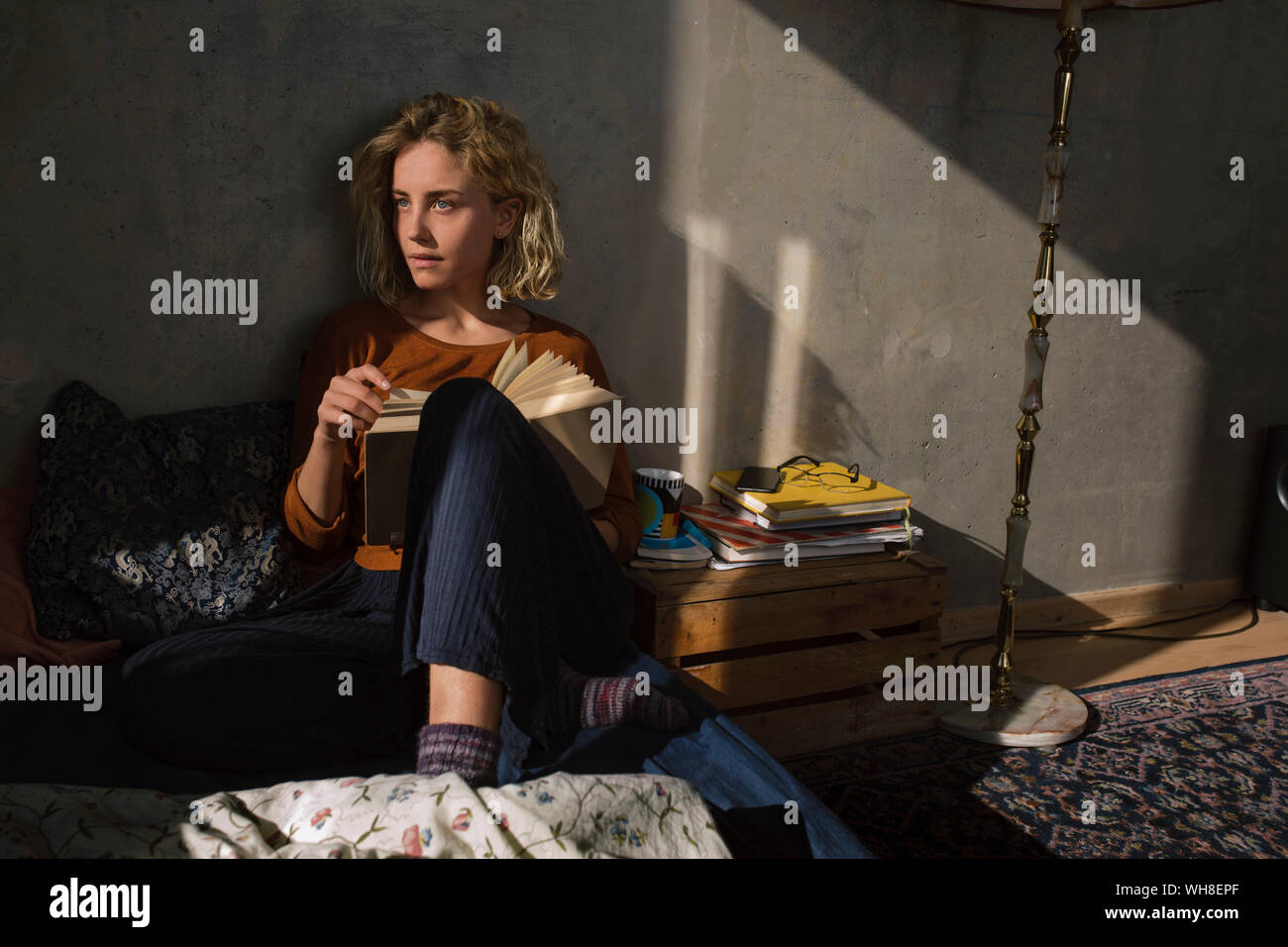 Pensive student sitting on bed with a  book Stock Photo