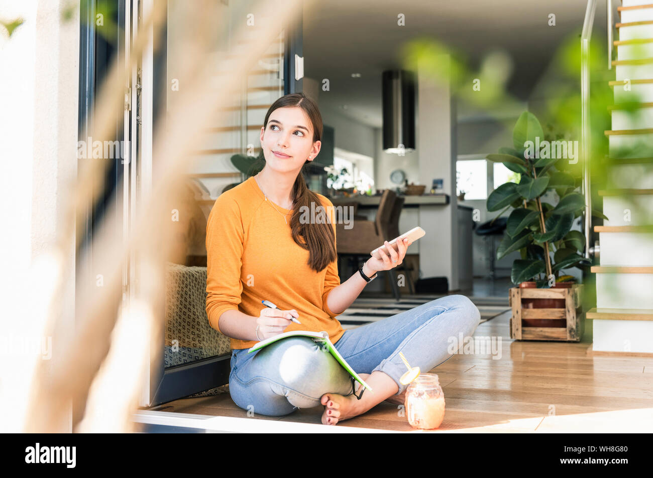 Young woman sitting with cell phone and notebook at terrace door Stock Photo