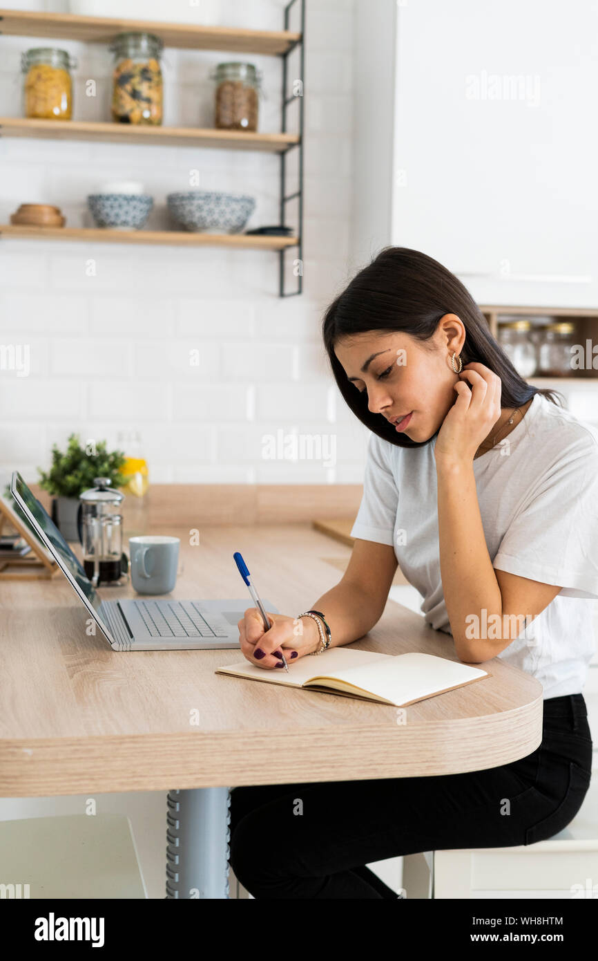 Young woman with laptop taking notes at home Stock Photo