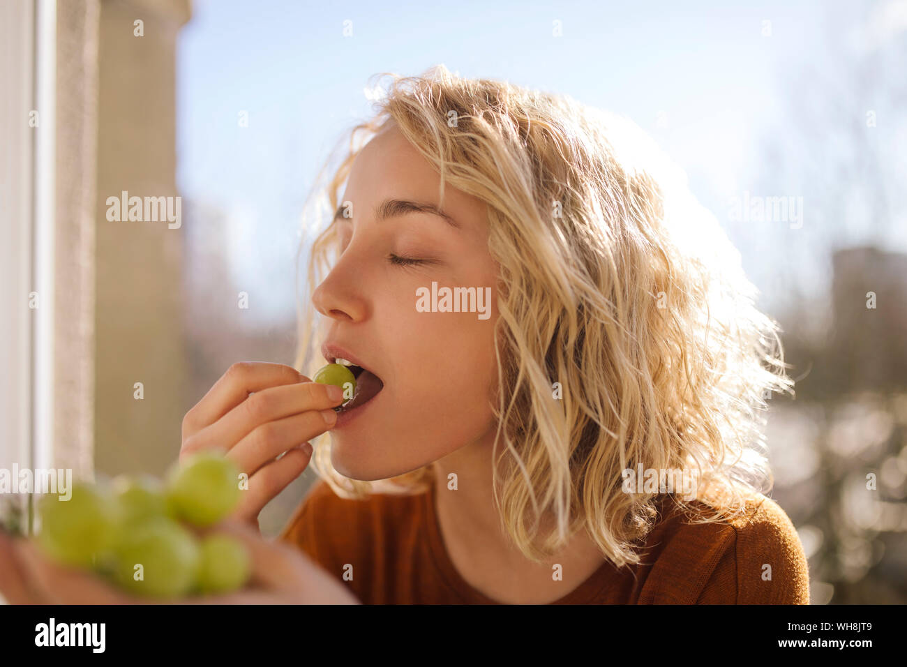 Portrait of blond young woman eating green grapes Stock Photo