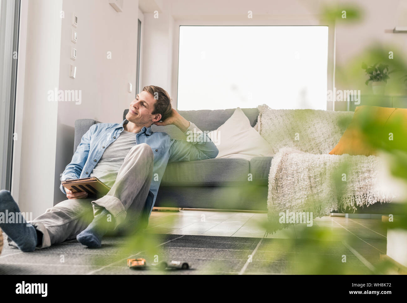 Mid adult man sitting on floor, using digital tablet Stock Photo