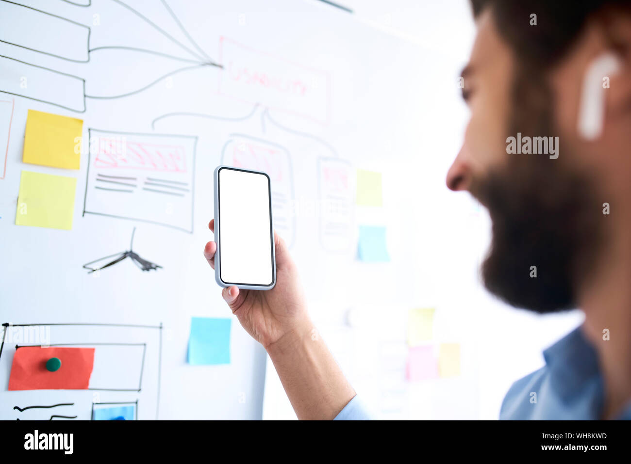 Businessman standing in front of a whiteboard and holding aloft his smartphone Stock Photo