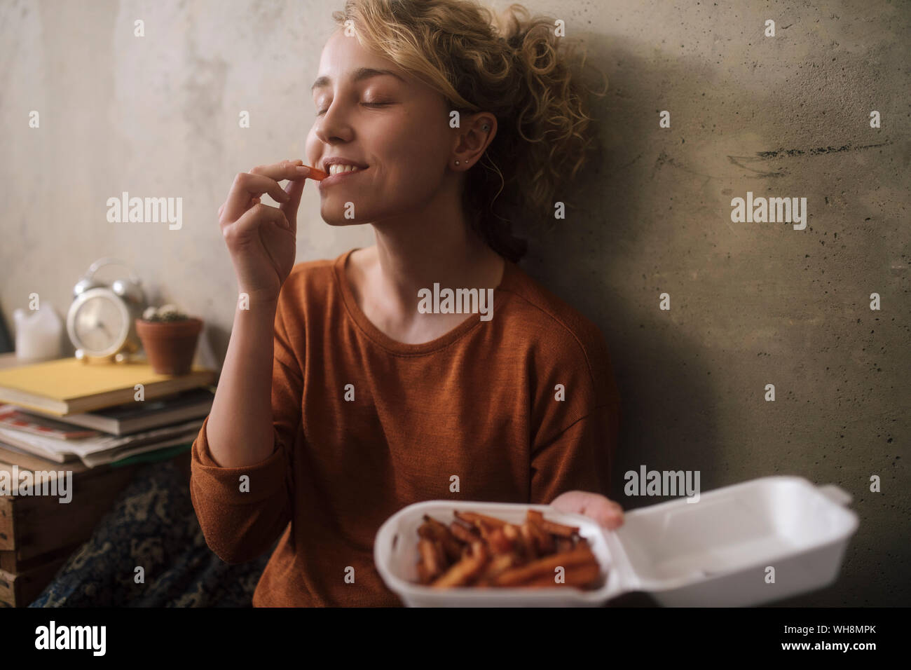 Portrait of young woman eating French Fries at home Stock Photo