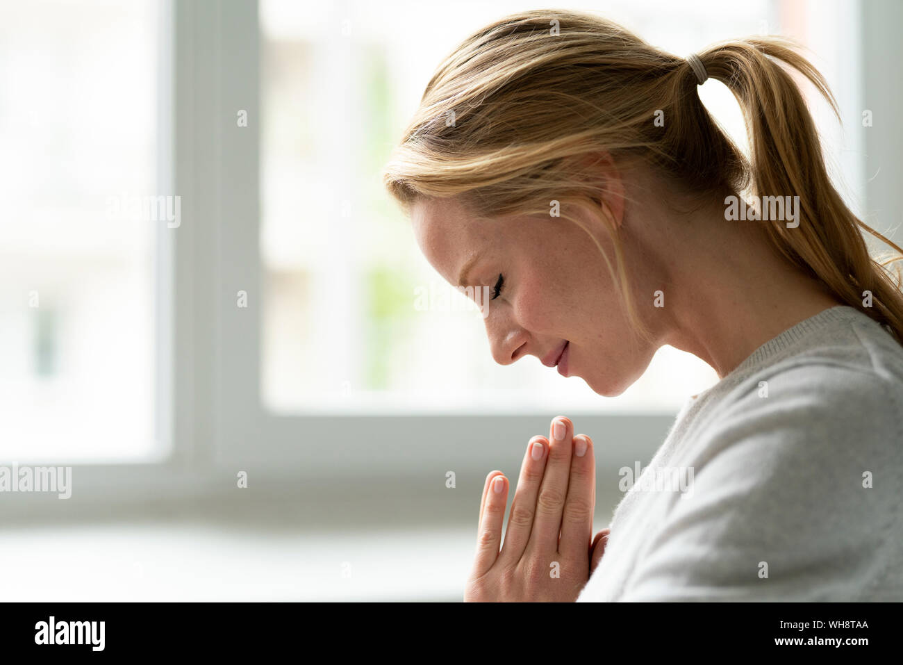 Smiling young woman with closed eyes and clasped hands Stock Photo