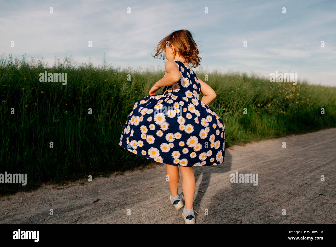 Back view of little girl wearing summer dress with floral design dancing on dirt track Stock Photo