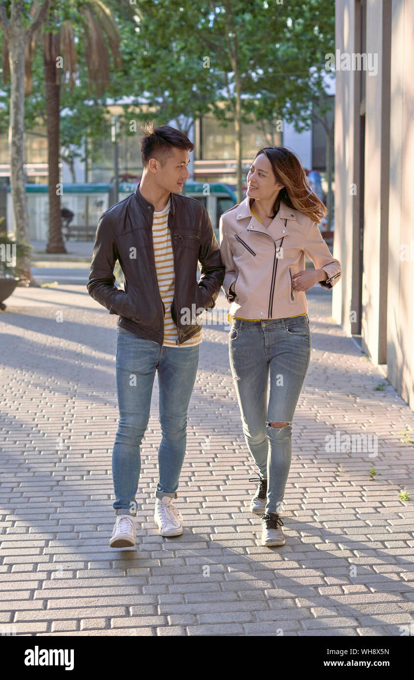 Couple wearing jeans and leather jackets walking on street in the evening Stock Photo