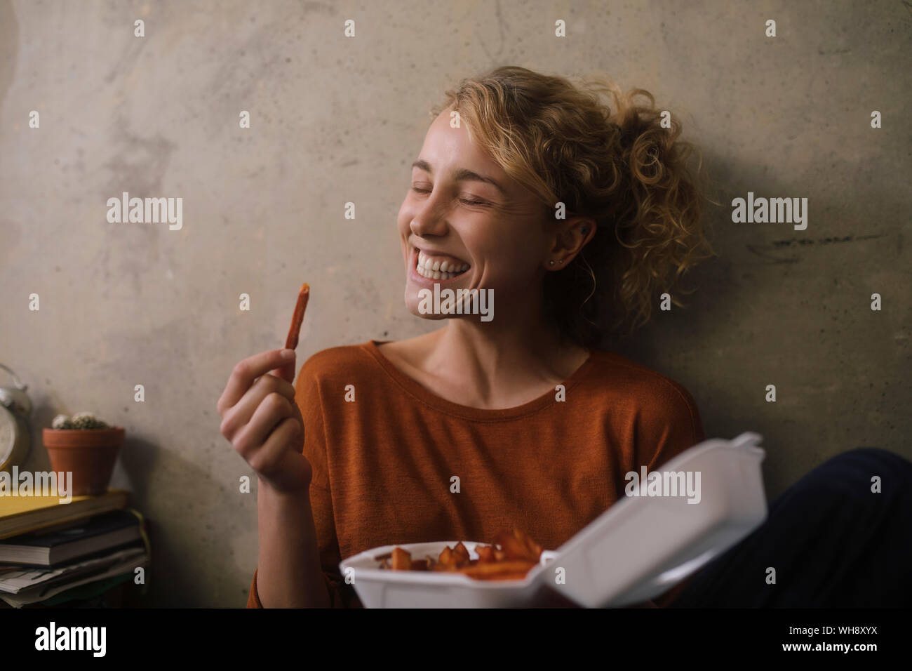 Portrait of grinning young woman eating French Fries at home Stock Photo