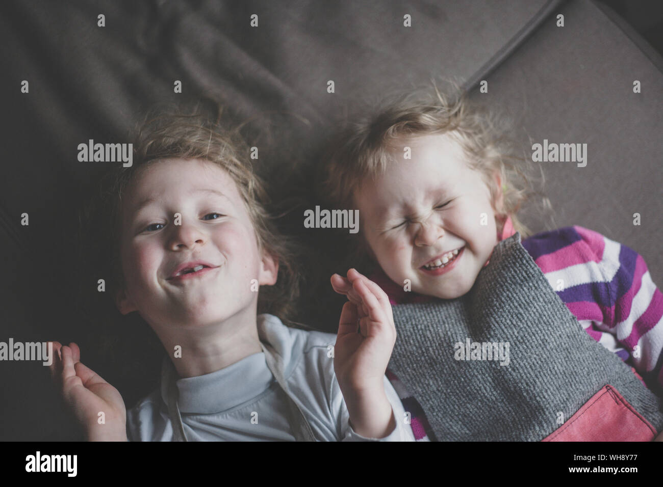 Portrait of two little sisters lying side by side on couch having fun, top view Stock Photo