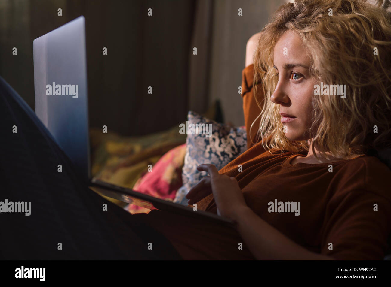 Portrait of blond young woman lying on bed using laptop Stock Photo