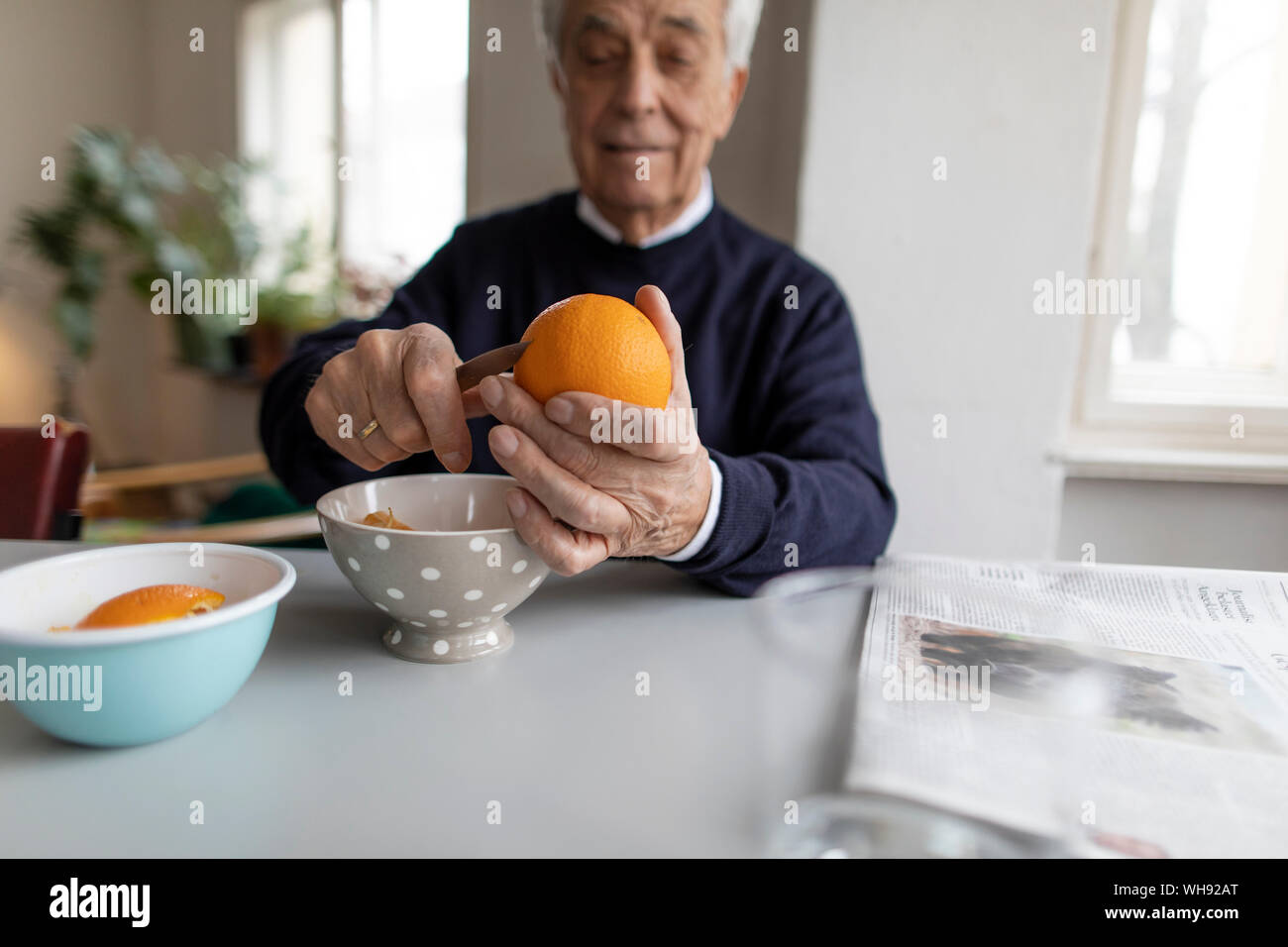 Senior man peeling orange at home Stock Photo