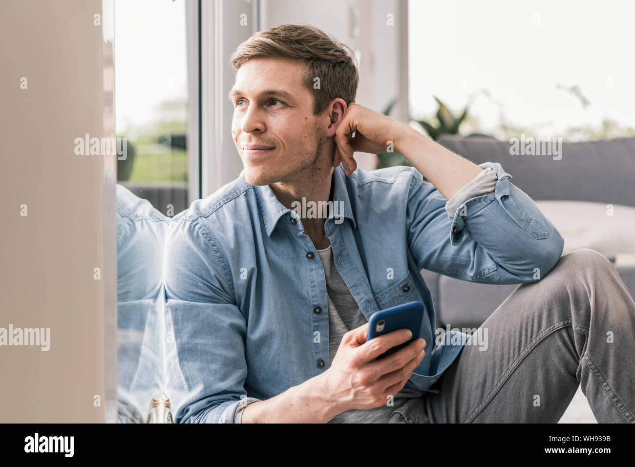 Mid adult man sitting by window, using smartphone Stock Photo