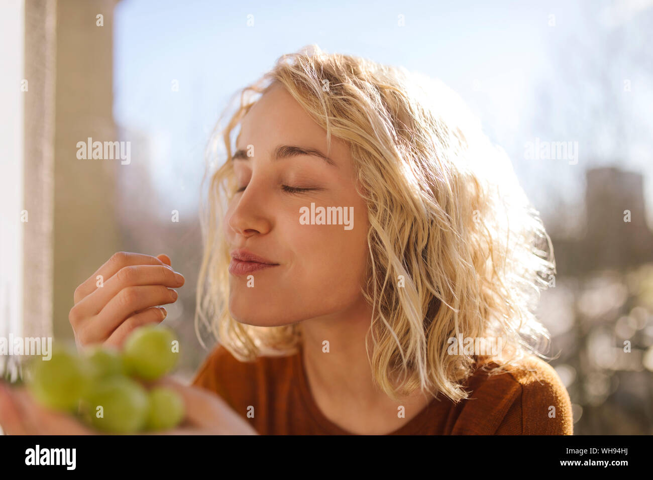 Portrait of blond young woman eating green grapes Stock Photo