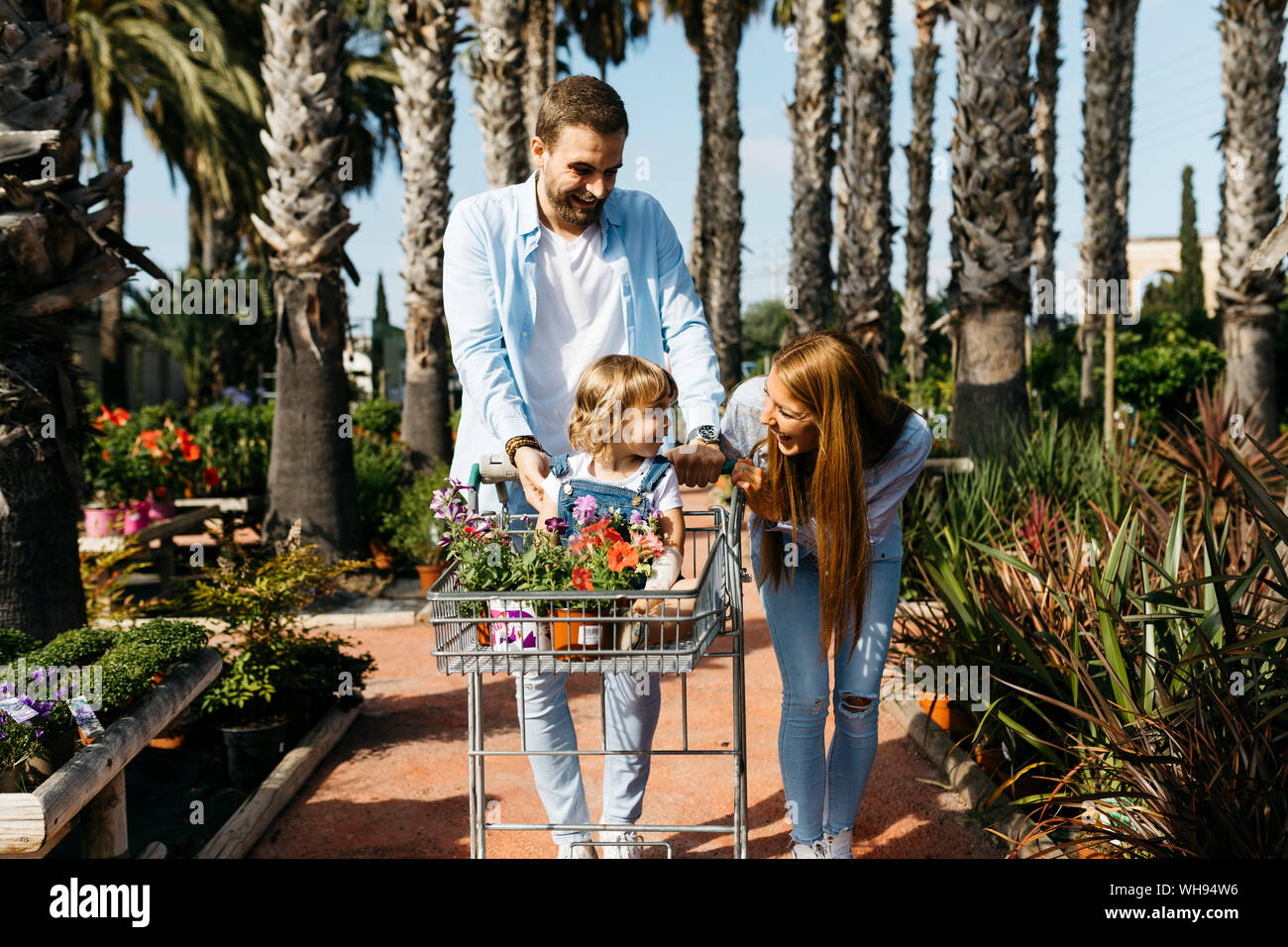 Happy family buying plants in a garden center wth the daughter in shopping cart Stock Photo