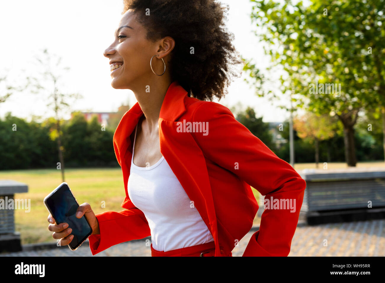 Smiling young woman with smartphone wearing fashionable red pantsuit Stock Photo