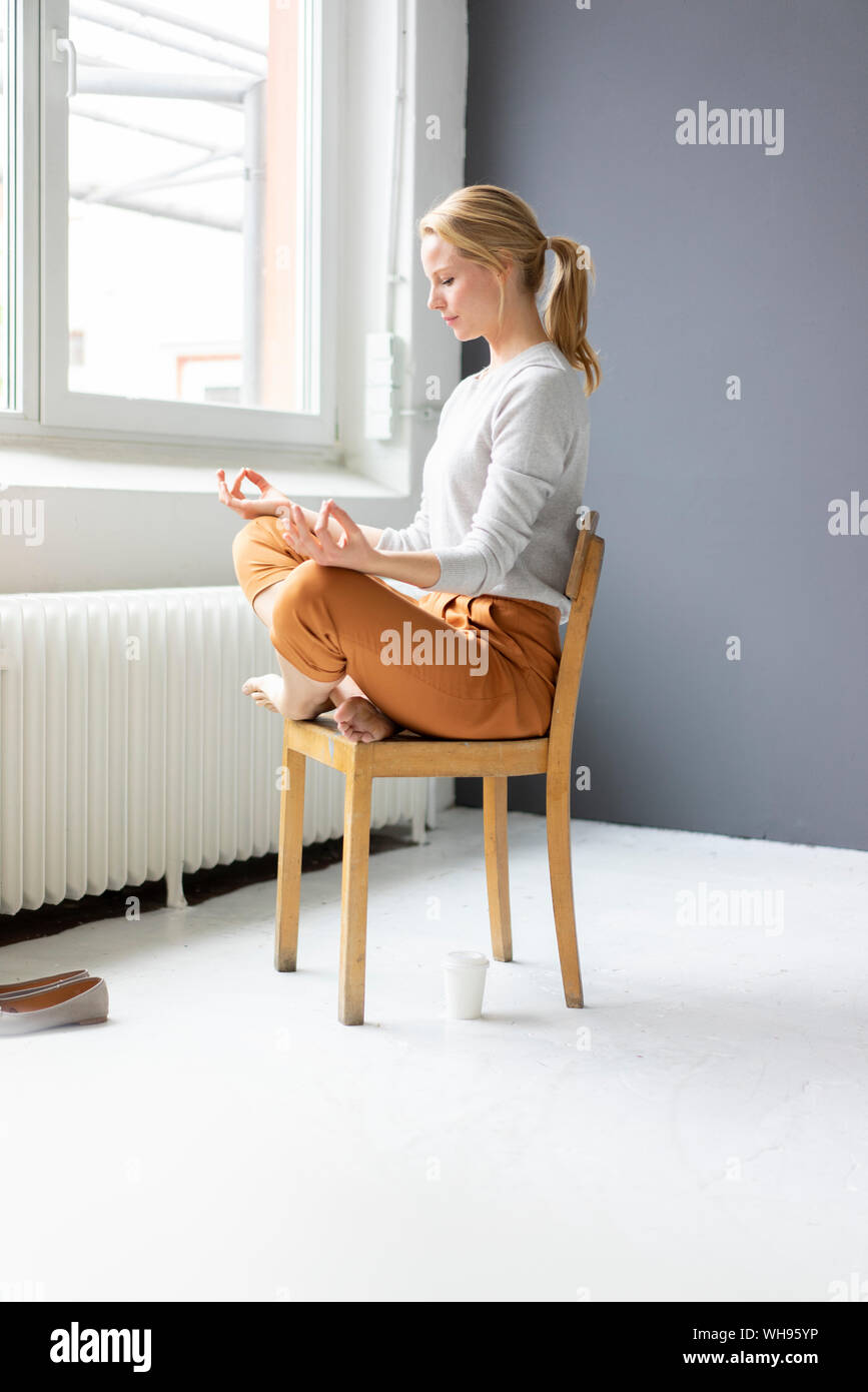 Young woman sitting on chair in office practicing yoga Stock Photo
