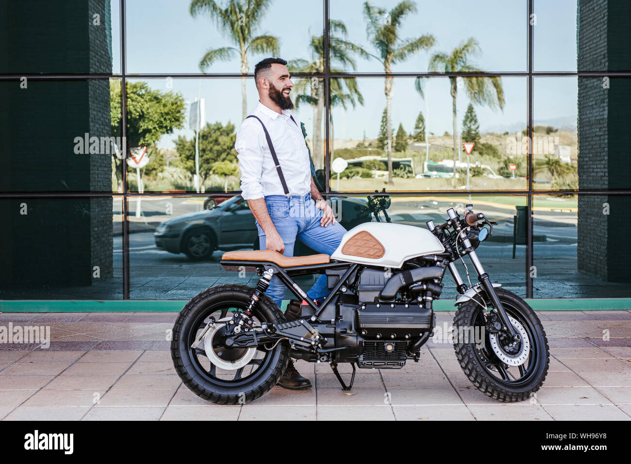 Man standing with motorbike standing in front of glass facade Stock Photo