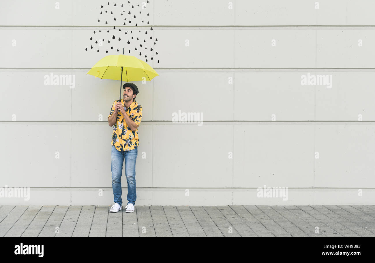 Digital composite of young man holding an umbrella at a wall with raindrops Stock Photo