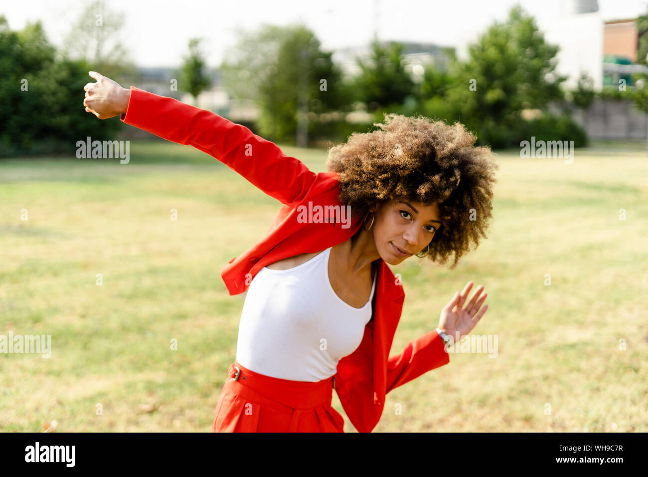 Portrait of moving young woman wearing fashionable red pantsuit and white top Stock Photo