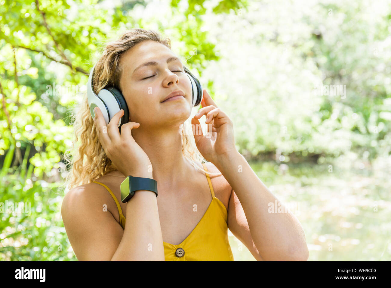 Smiling woman with closed eyes listening to music at lakeside Stock Photo